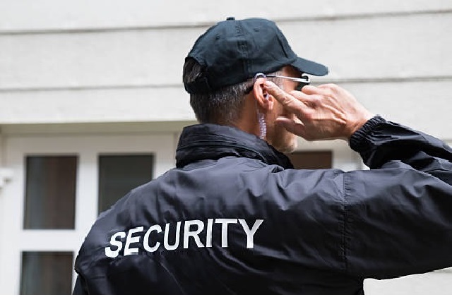 Rear view of mature security guard listening to earpiece against building